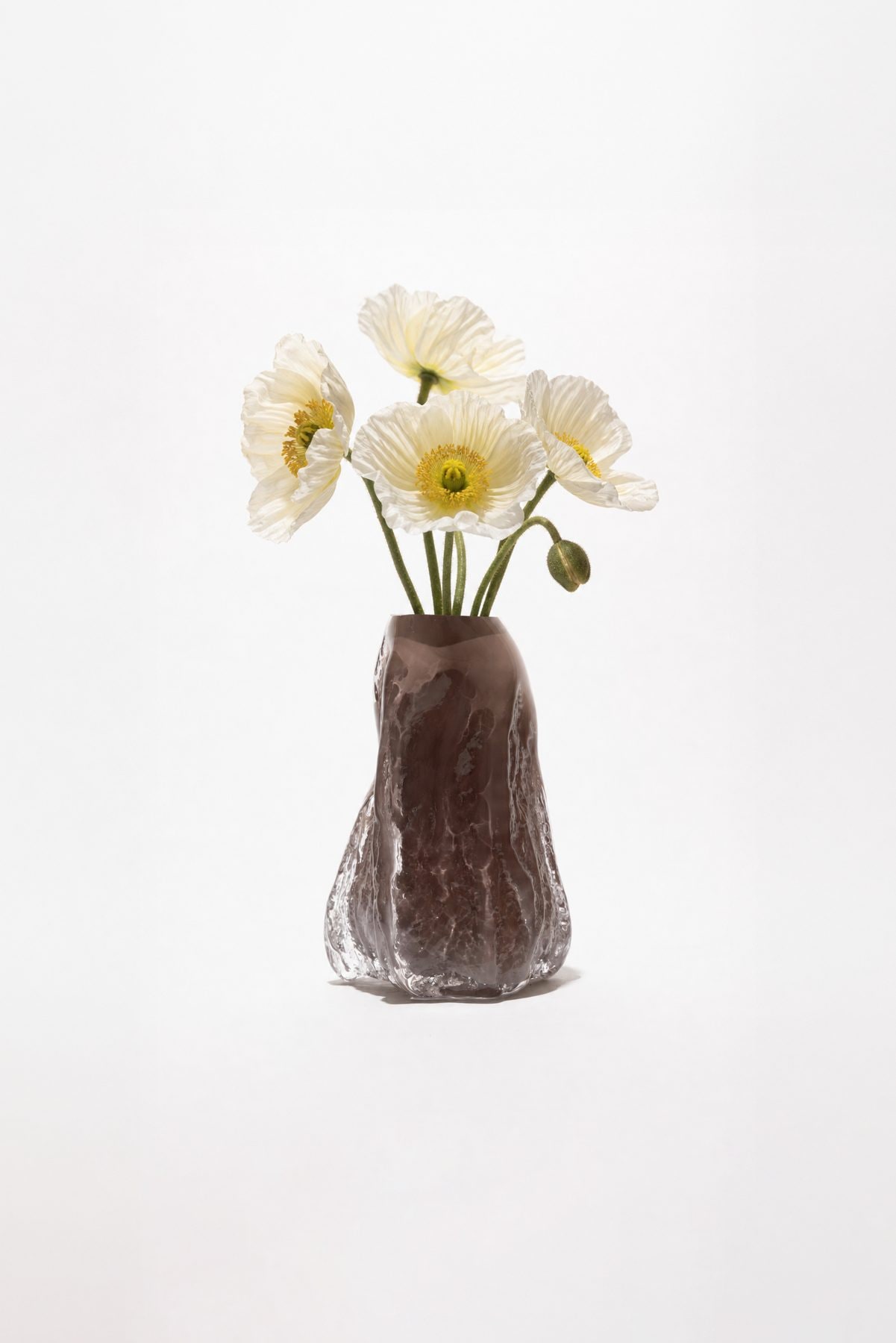 The cast-glass vase holding white poppies, on white